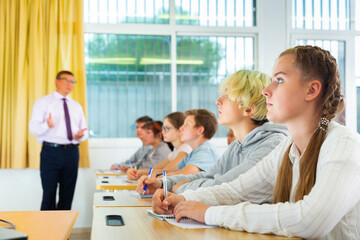 Multiracial group of teenage students working at class, listening explanations of teacher in classroom