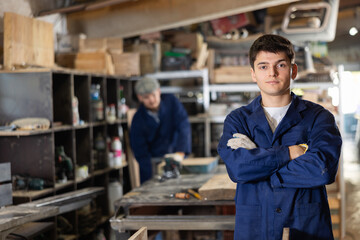 Young male carpenter in uniform posing in wood workshop