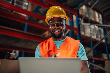 Smiling warehouse worker using laptop for inventory management