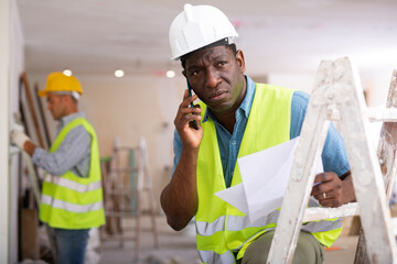 African-american man builder having telephone conversation, discussing project documentation, repair works in apartment.