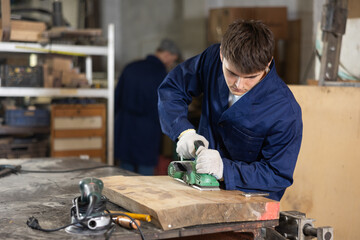 Man using electric planer on wooden plank at the workshop