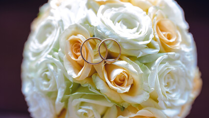 Close-up of two wedding rings resting on a bouquet of white and yellow roses, symbolizing love and commitment.