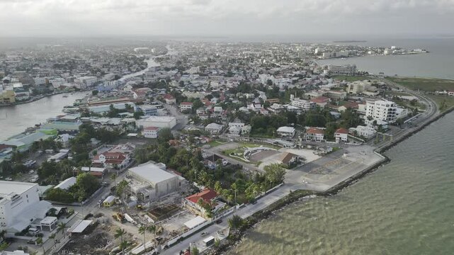 Drone flies north high over Belize City just before a sunset on cloudy afternoon