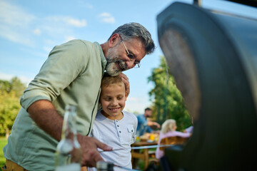 Grandfather embracing grandson while grilling at family barbecue party