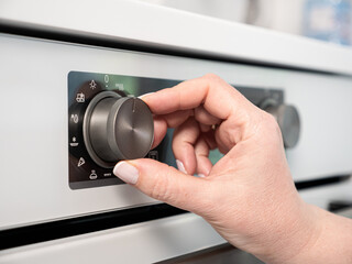 Woman adjusting modern white oven in kitchen.  Female hand pushing and turning knobs on oven control panel