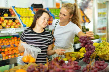 Two positive woman choosing sweet fresh grape at grocery section of supermarket