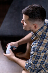 A man sits comfortably on a couch, holding a game controller