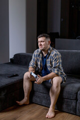 A man sits comfortably on a couch, holding a game controller