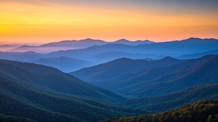 Fototapeta premium Serene sunset over layered blue mountains, hazy atmosphere.