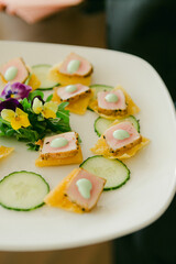 Gourmet appetizer featuring cucumber, floral garnish, and flavorful toppings served on a white plate at an elegant gathering