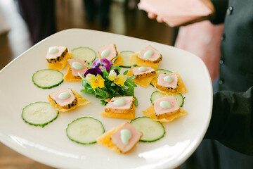 Catered appetizer platter featuring elegantly arranged bites with cucumber slices and edible flowers at a formal event