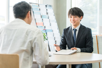 男性顧客を接客・商談・カウンセリングする若いアジア人ビジネスマン（保険・自動車）
