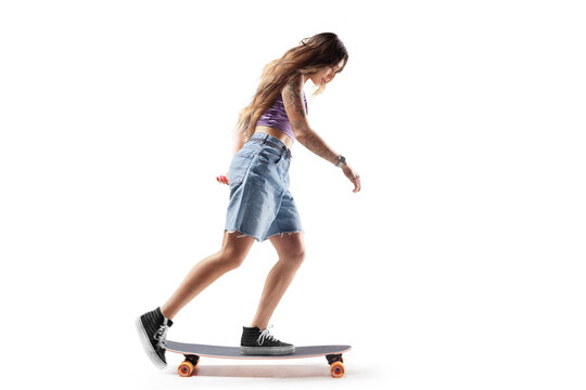 Skateboard. Side view. Charming young girl riding a skateboard. Extreme sports. Young woman riding a skateboard and doing tricks. Sport in action. Isolated