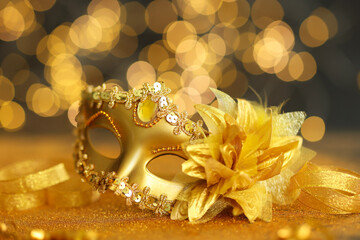 Beautiful carnival mask on golden shiny surface against blurred lights, closeup