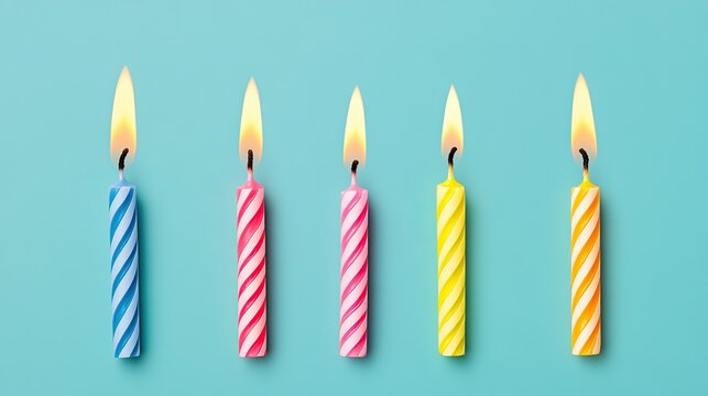 Colorful birthday candles with flames arranged in a row against a pastel blue background