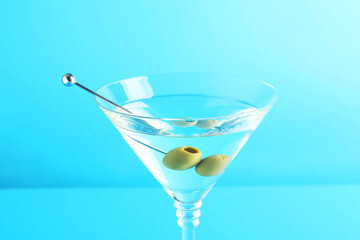 Martini cocktail with olives in glass on light blue background, closeup