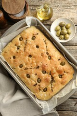 Delicious focaccia bread with olives, thyme, salt and oil on wooden table, flat lay