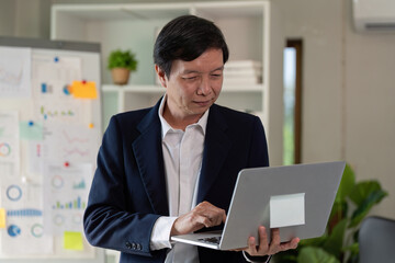 Elderly professional using a laptop while standing in a modern office.