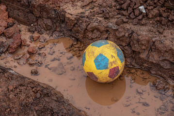 A dirty soccer ball is sitting in a muddy puddle