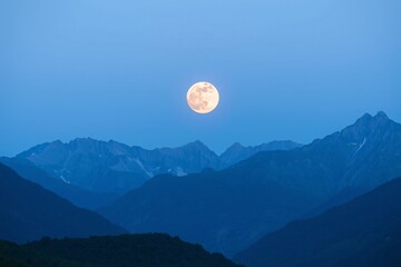 A peaceful mountain range scene at night, featuring a luminous full moon. Highlights tranquility, natural beauty, and a connection with nature under a serene and clear sky.