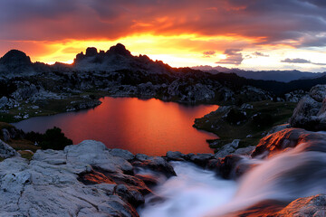 Breathtaking sunset over a mountain lake, reflecting vibrant colors.  Waterfall flows into foreground.