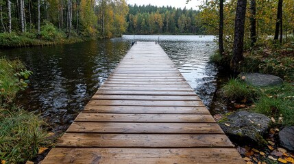 Fototapeta premium Wooden pier extends into a calm lake surrounded by autumn forest during daytime.