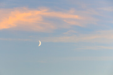 Crescent moon and pastel clouds at dusk in a tranquil sky