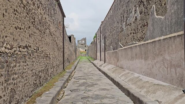 Pompeii ruins-View over ancient Roman road between parallel stone walls - Zoom to distant building