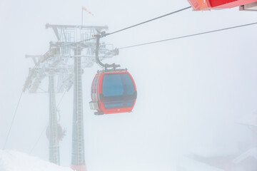 Red cable car in foggy weather on snowy mountain