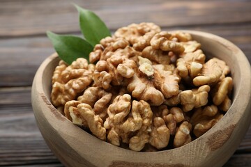 Peeled walnuts and green leaves in bowl on table, closeup