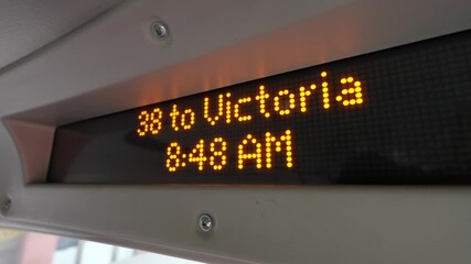 A digital display inside a city bus shows the route 38 to Victoria at 8:48 AM, This technology enhances the commuting experience by offering real-time updates on the route and schedule. - Powered by Adobe