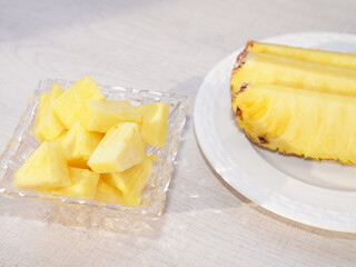 Piece of pineapple in glass bowl on white wood background.