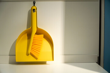 Broom and dustpan are a pair of cleaning tools. Plastic hand broom and yellow scoop on room background