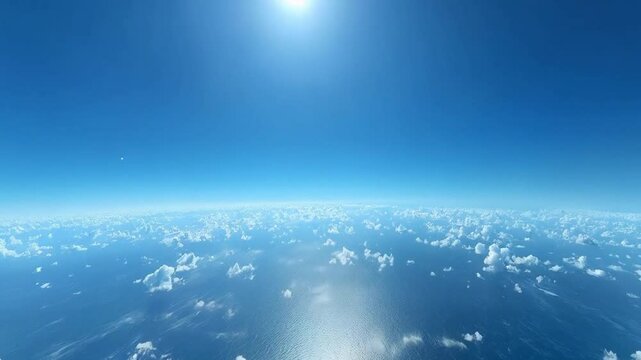 High angle view of a vast expanse of deep blue ocean dotted with fluffy white clouds against a vibrant blue sky, with bright sunlight visible