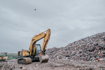 Obraz premium A large, worn-out excavator is stationed at a landfill, surrounded by towering piles of waste. 