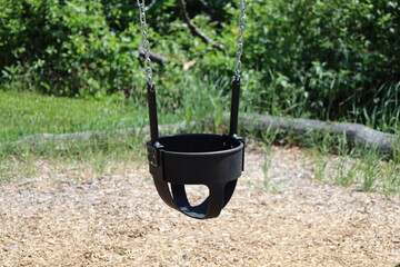 close-up rubber basket suspended on chains above sand forms young child swing in summer sunshine