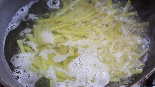 Close-up of flat noodles boiling in a karahi on a kitchen stove.