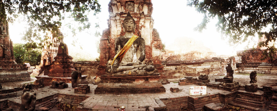 Panoramic view of Large Buddha statue adorned with cloth and flowers in the Ancient ruins of Ayutthaya historical park in Ayutthaya, Thailand.