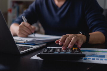 Businessman using a calculator and writing financial data. Budget planning, accounting, tax calculation, expense tracking, and financial management for corporate and personal finance.