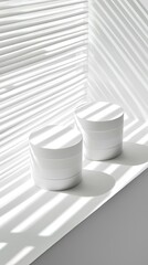 Two white containers on a windowsill with dramatic light and shadow patterns creating a serene atmosphere