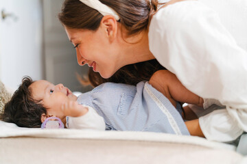 Mother interacting and playing with her baby girl lying on bed