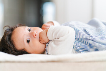 Baby girl sucking fingers while relaxing on bed