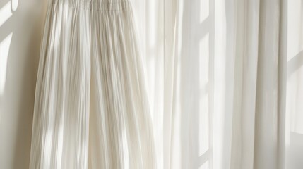 Cream pleated skirt hangs near sheer curtains. Sunlight filters through, creating soft shadows, ideal for fashion or texture themes.