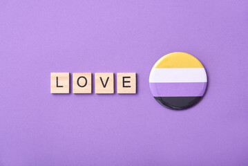 Wooden word Love beside a flag badge symbol of non binary community.