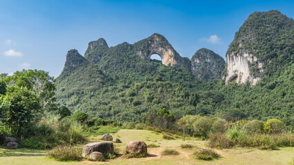 Beautiful mountain landscape. A round hole at the top. Green vegetation on the slopes. Picturesque boulders in a clearing in the valley. China. Yangshuo Moon Hill © Вера 