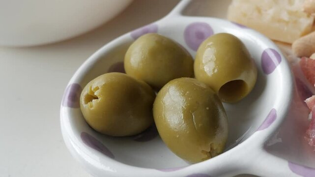 Olives served in a small dish, a part of a tapas platter with jamon, cheese, and chips