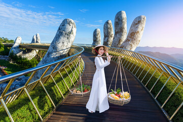 Young female tourists in Ao Dai dresses carry fruit baskets on a bridge.