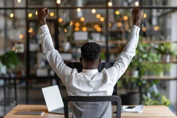 Excited Young Businessman Celebrating Success at Desk with Arms Raised