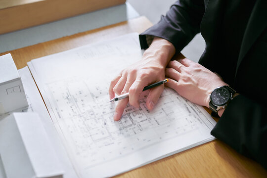 建築の模型を前に建物の設計図を見て確認申請の図面のチェックをする建築士の男性の手元