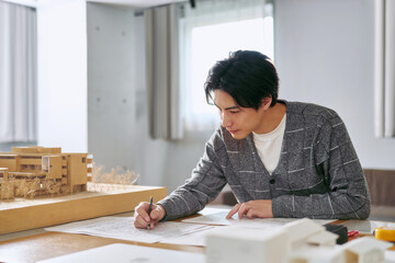 建築模型を横に大規模な不動産開発の為の計画図を書く建築士の1人の男性